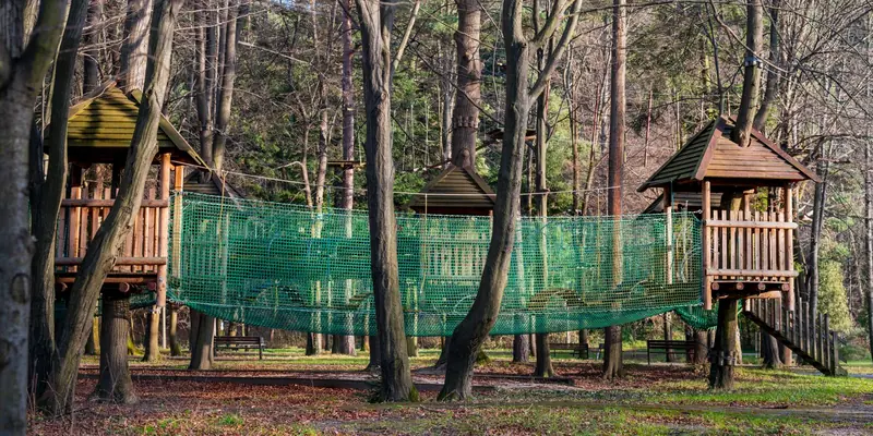Symbolbild: Baumhäuser mit grüner Netzbrücke auf einem Waldspielplatz