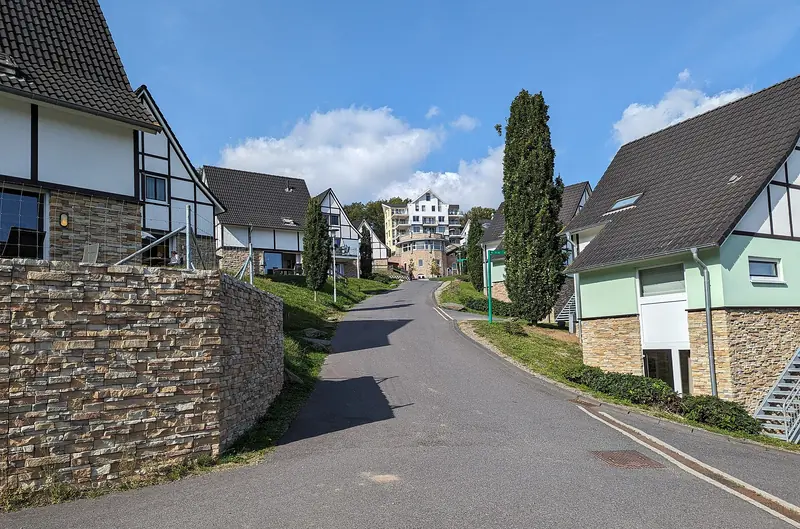 Autofreie Straße zwischen Ferienhäusern mit Steinsockel, am Ende ein Rundgebäude mit Apartments