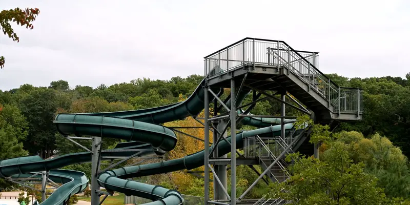 Symbolbild: Grüne Riesenrutsche mit Treppenturm vor einem Laubwald