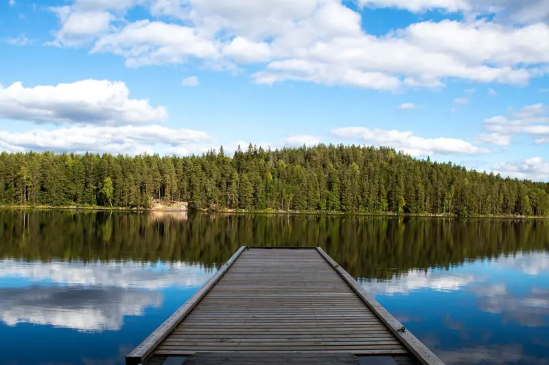 Symbolbild: Holzsteg in einem spiegelglatten Waldsee unter Schäfchenwolken