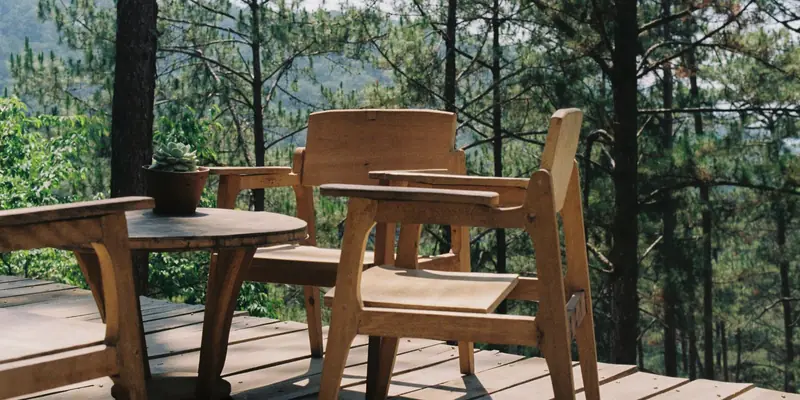 Symbolbild: Holzterrasse mit Tisch und Stühlen vor einem Kiefernwald